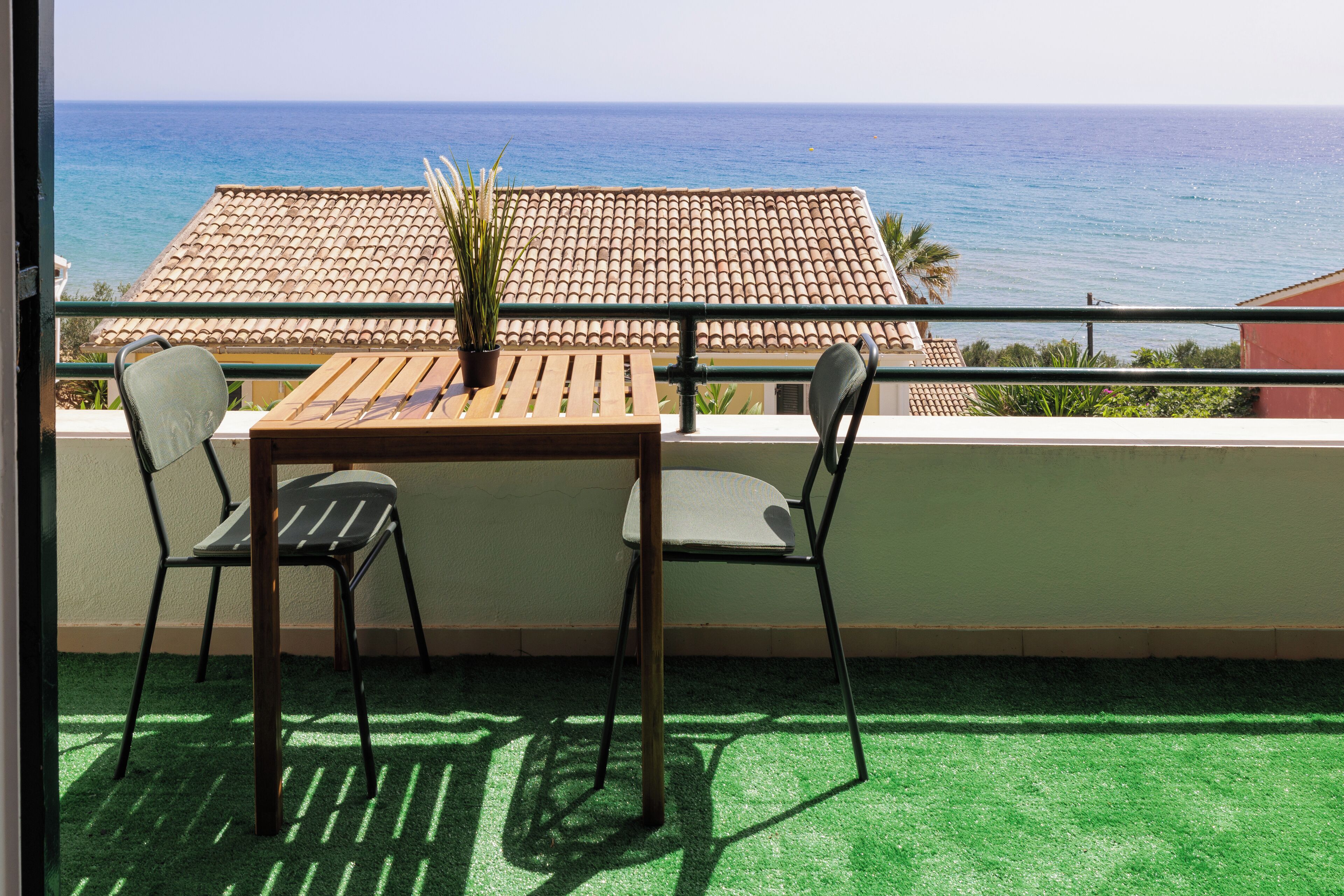 Un balcon avec une table et des chaises, une plante en pot et une vue sur la mer.