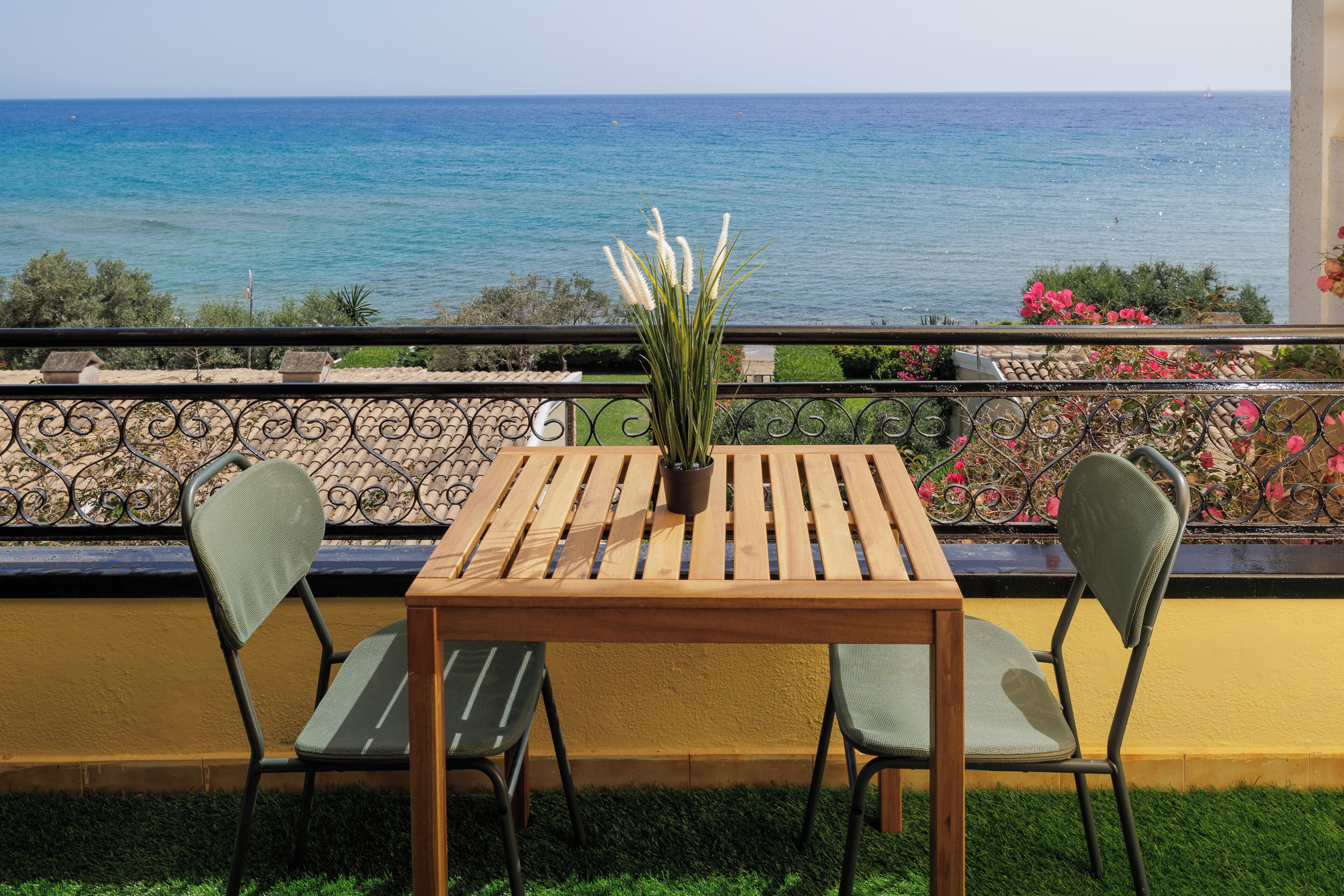 A wooden table with two chairs and a potted plant, overlooking a coastal view.