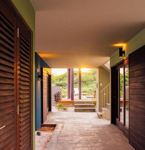 Passadís modern amb sòl de formigó, portes de fusta i vista d'un jardí amb escales que condueixen a l'exterior.