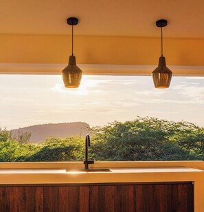 A kitchen with a sink, two pendant lights, and a view of greenery and hills.