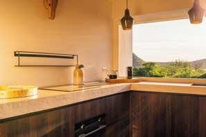 A kitchen with a wooden countertop, a hanging light fixture, and a view of greenery outside.