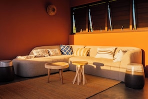 A cozy living room with a sofa, two small wooden tables, and a large window with blinds. - Luxe Villa Bliss met privézwembad, nabij strand, Willemstad en voorzieningen (Sint Michiel)