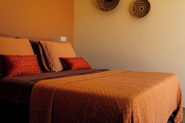 A bed with a brown quilt and red pillows, a bedside table, and a wall-mounted light switch.
