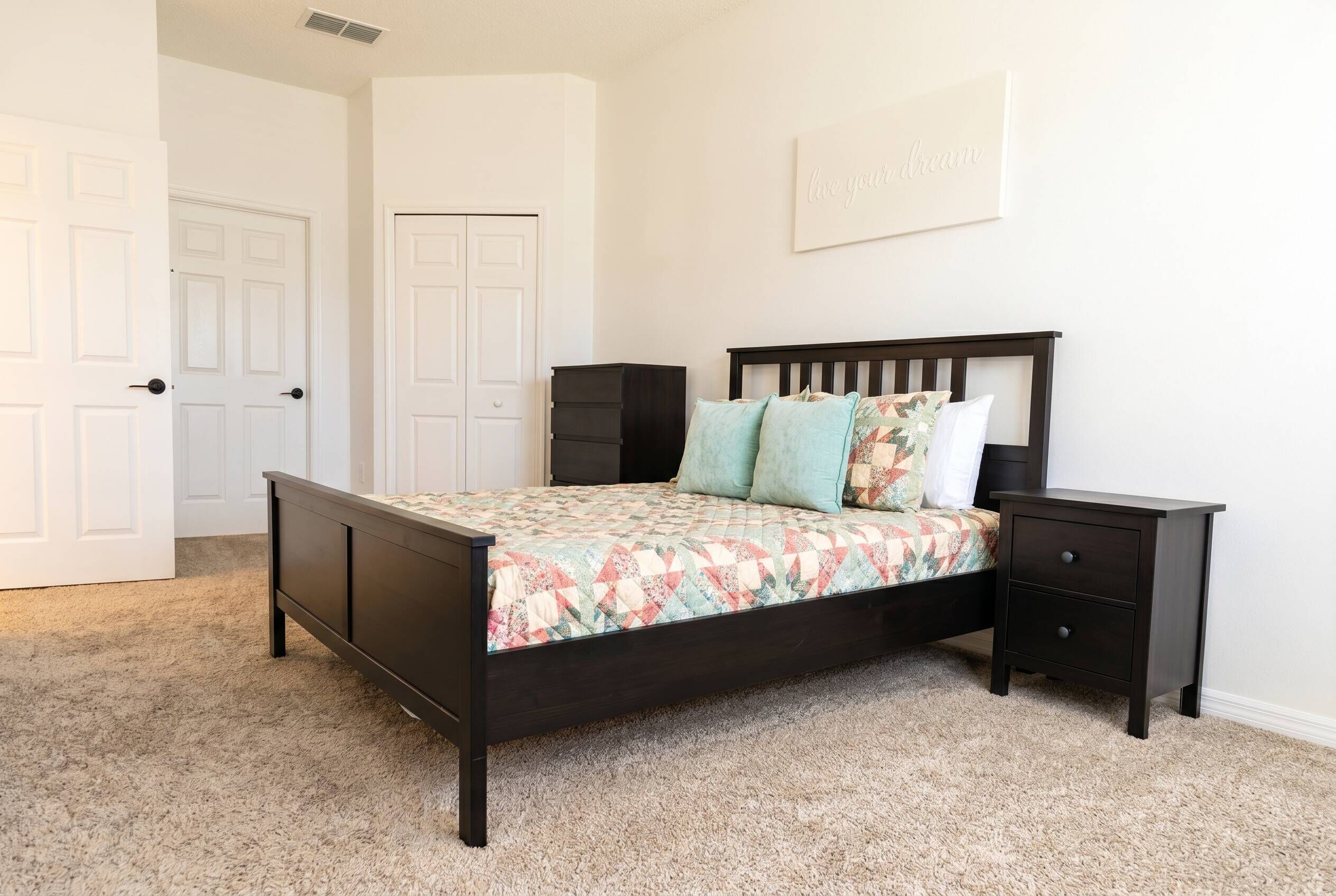 Un dormitorio con cama, mesitas de noche, cómoda y puerta.
