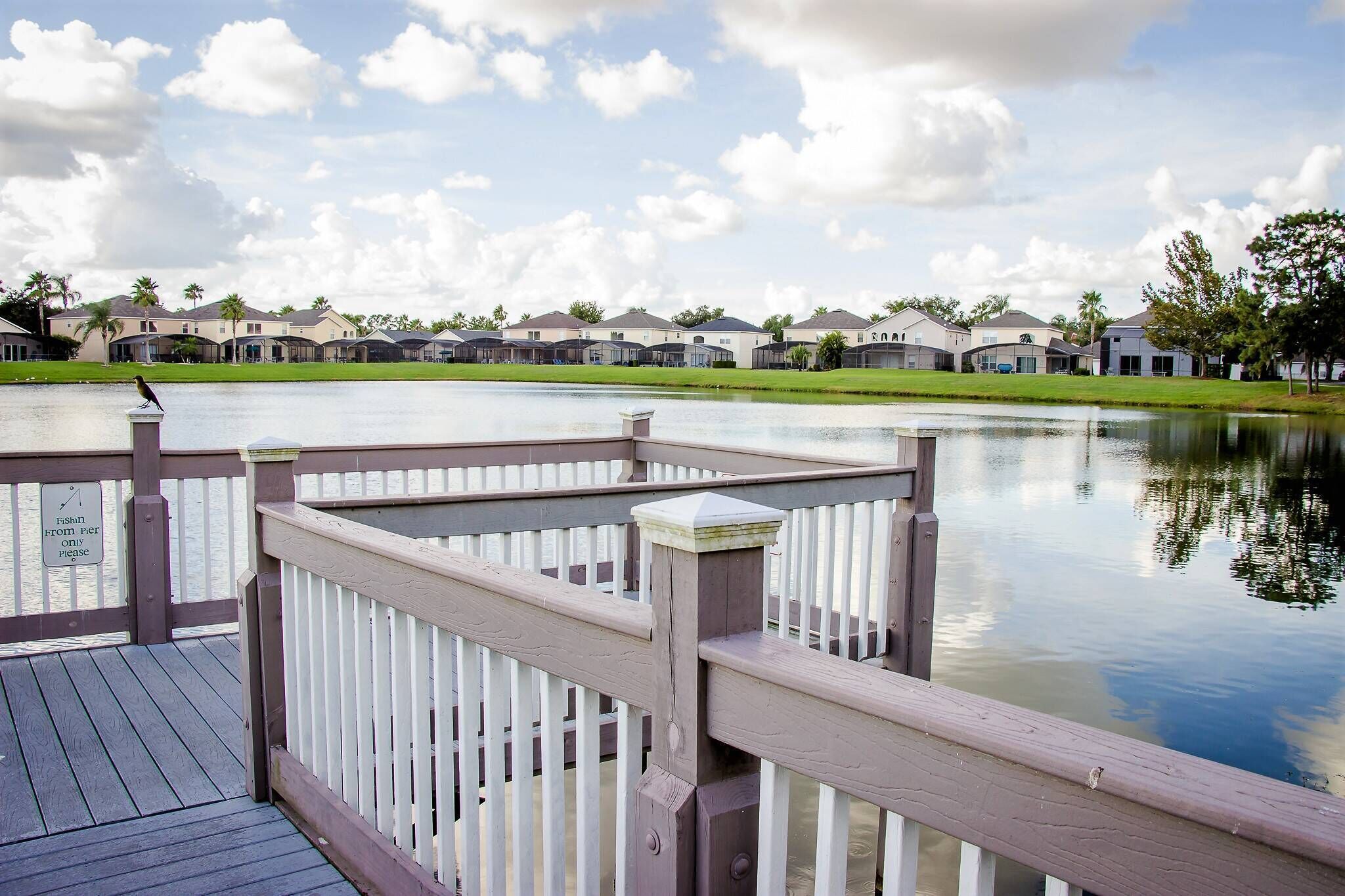A wooden deck with a railing overlooking a calm body of water, with houses in the background.
