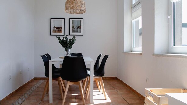 A dining area with a white table, black chairs, a woven pendant light, and two framed pictures on the wall.