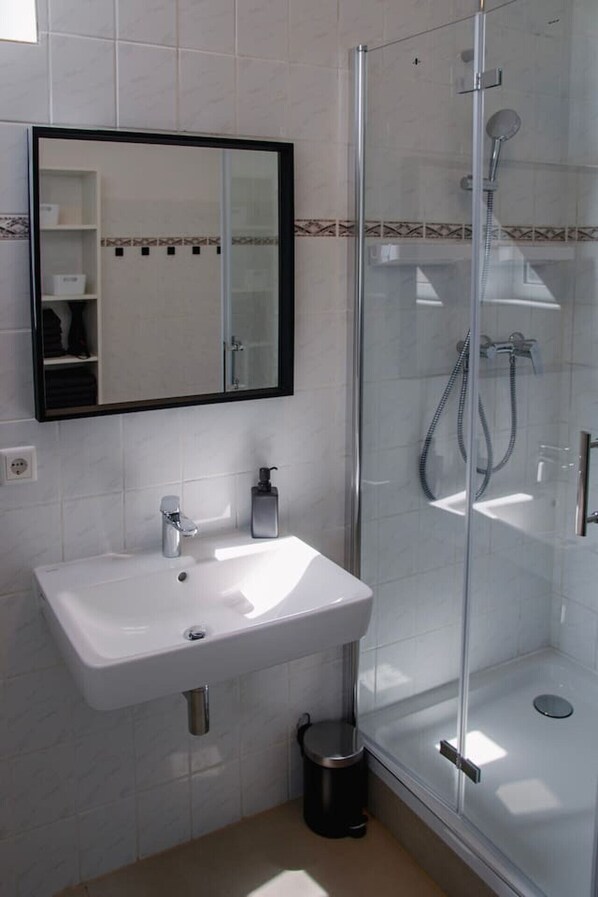 A modern bathroom with a white sink, a mirror, and a glass-enclosed shower.