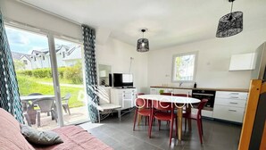 A modern bedroom with a large bed, a dining area with a table and chairs, and a kitchen area. - Maisonnette tout confort - Golf - Piscine (Quéven)
