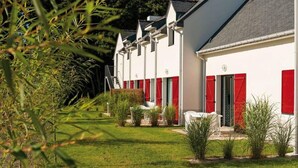 A row of white buildings with red shutters, a grassy lawn, and a staircase leading to the entrance. - Maisonnette tout confort - Golf - Piscine (Quéven)