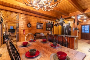 A wooden interior with a dining table set for four, a kitchen area with modern appliances, and a large chandelier. - 2 Cubs Cabin (Blowing Rock)