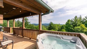 Terraza de madera con jacuzzi y parrilla, con vista a un paisaje montañoso.