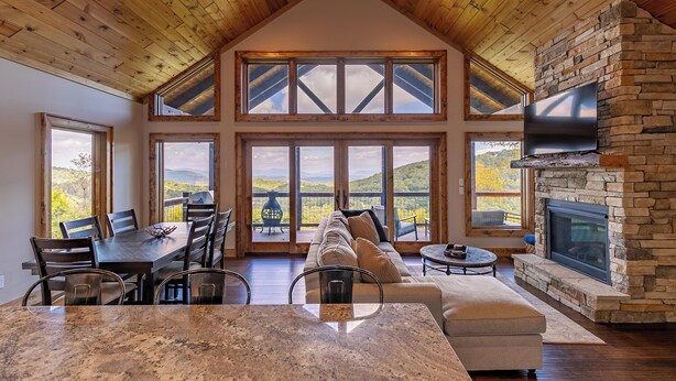 En rummelig opholdsstue med højt til loftet, store vinduer, en stenspejs og et hyggeligt siddeområde.