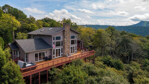 A two-story house with a stone chimney, large windows, and a deck with outdoor seating. - Chalet at The Summit of Beech (Banner Elk)