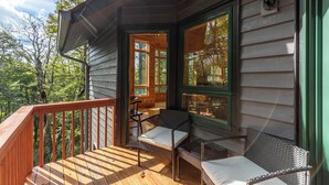 A wooden deck with a railing, a table, and two wicker chairs. - Chalet at The Summit of Beech (Banner Elk)
