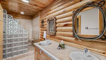 A bathroom with wooden log walls, two sinks, a mirror, and a glass shower enclosure.