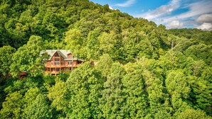 A large, rustic log cabin surrounded by dense forest. - A High Country Retreat (Boone)