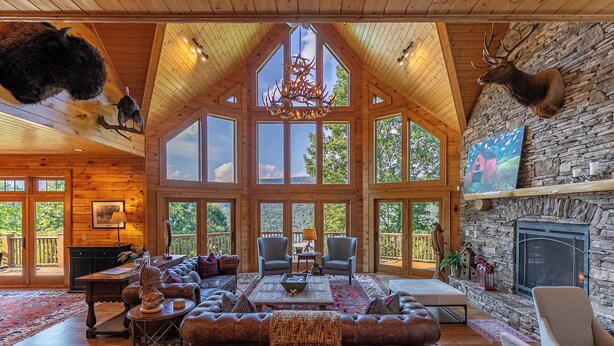 A spacious living room with a large fireplace, wooden ceiling, and a stone wall. - A High Country Retreat (Boone)