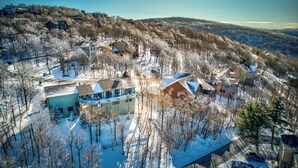 An aerial view of a residential area with houses surrounded by snow-covered trees and hills in the background. - Hill Station (Banner Elk)