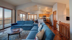 A spacious living room with a large blue sofa set, a dining area with a table and chairs, and a kitchen with wooden cabinets and stainless steel appliances. - Hill Station (Banner Elk)