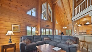 Un intérieur de chalet chaleureux avec un grand canapé d’angle, une table à manger en bois et un coin cuisine.