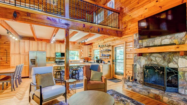 A spacious log cabin interior with a dining area, a living room with a fireplace, and a kitchen.
