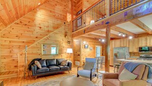 A spacious wooden cabin interior with a living area, a balcony, and a kitchen.