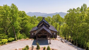 A lodge with a triangular roof and a stone foundation, surrounded by a forest with a gravel driveway leading to the entrance. - Sanctuary at Eagles Nest (Banner Elk)