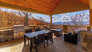 Une terrasse extérieure équipée d’un barbecue, de sièges et offrant une vue sur les arbres et les montagnes aux couleurs automnales.