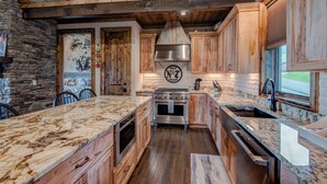 A kitchen with wooden cabinets, a stone wall, and a large island with a marble countertop. - Lucky 7 at Eagles Nest (Banner Elk)
