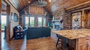A spacious living area with a stone fireplace, wooden ceiling, and a large window overlooking a deck. - Lucky 7 at Eagles Nest (Banner Elk)