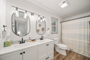 A bathroom with a white sink, mirror, and toilet, a shower curtain, and a ceiling light fixture. - A Red Chalet (Newland)