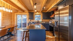 A modern kitchen with wooden beams, a large island, stainless steel appliances, and a view of the outdoors. - Ursa Minor (Banner Elk)