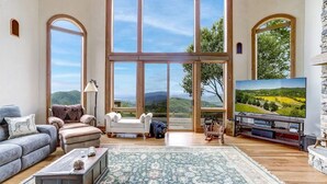 A spacious living room with large windows, a comfortable sofa, a television, and a coffee table. - Sunrise to Sunset (Hayesville)
