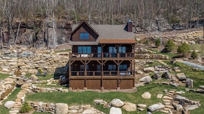 A multi-story wooden cabin with a stone foundation, surrounded by a natural landscape. - SkyFall at Eagles Nest (Boone)