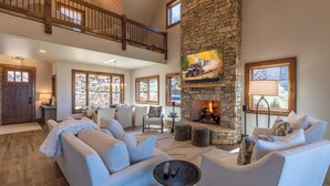 A spacious living room with a stone fireplace, comfortable seating, and a high ceiling with wooden beams. - SkyFall at Eagles Nest (Boone)