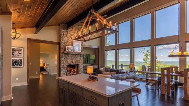 A spacious kitchen with a large island, stone fireplace, and a view of the outdoors through large windows. - Sweet Sejour (Deep Gap)