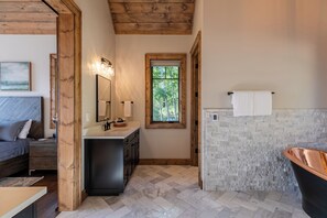 Un bagno con soffitto in legno, parete in pietra, vasca da bagno nera e finestra vista alberi.