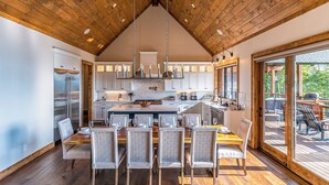 A spacious kitchen with a high wooden ceiling, a central island, and a dining area with chairs and a table. - Up and Away at Eagles Nest (Banner Elk)