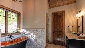 A bathroom with a freestanding bathtub, a wooden door, and a window with a view of trees. - Up and Away at Eagles Nest (Banner Elk)