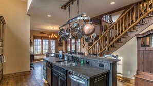 Une cuisine spacieuse avec un grand îlot central, un escalier en bois et un porte-casseroles suspendu.