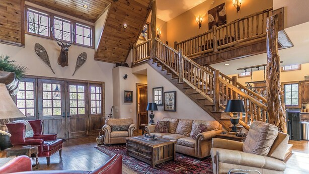 Un salon spacieux avec un plafond haut, des poutres en bois, un escalier et une grande fenêtre.