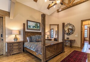 A spacious bedroom with a four-poster bed, wooden nightstands, a red rug, and a large mirror. - Elk Camp Lodge (Newland)