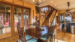 Une salle à manger spacieuse, dotée d’une grande table et de chaises en bois, d’un lustre et d’un escalier menant à un niveau supérieur.