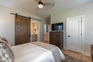 A bedroom with a bed, a wooden wardrobe, a TV on a stand, and a door. - Blue Meadows at Blue Ridge Mountain (Lenoir)