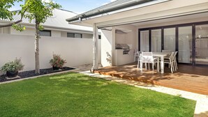 Un patio moderno con terraza de madera, una mesa de comedor con sillas y una parrilla.