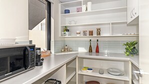 Cocina moderna con armarios blancos, microondas integrado y una variedad de utensilios y artículos de cocina.
