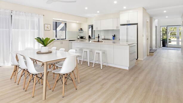 Una cocina moderna con armarios blancos, una isla central y un comedor con mesa y sillas blancas.