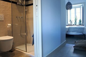Enjoy a clean and minimalist bathroom with a glass-enclosed shower, toilet, and sink, adjacent to a cozy bedroom with a bed and natural views.