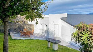 A white-walled building with a stone wall and a small pool. There is a table and chairs outside. - The Cliffs - La Maison du Puits (Porto do Barqueiro)