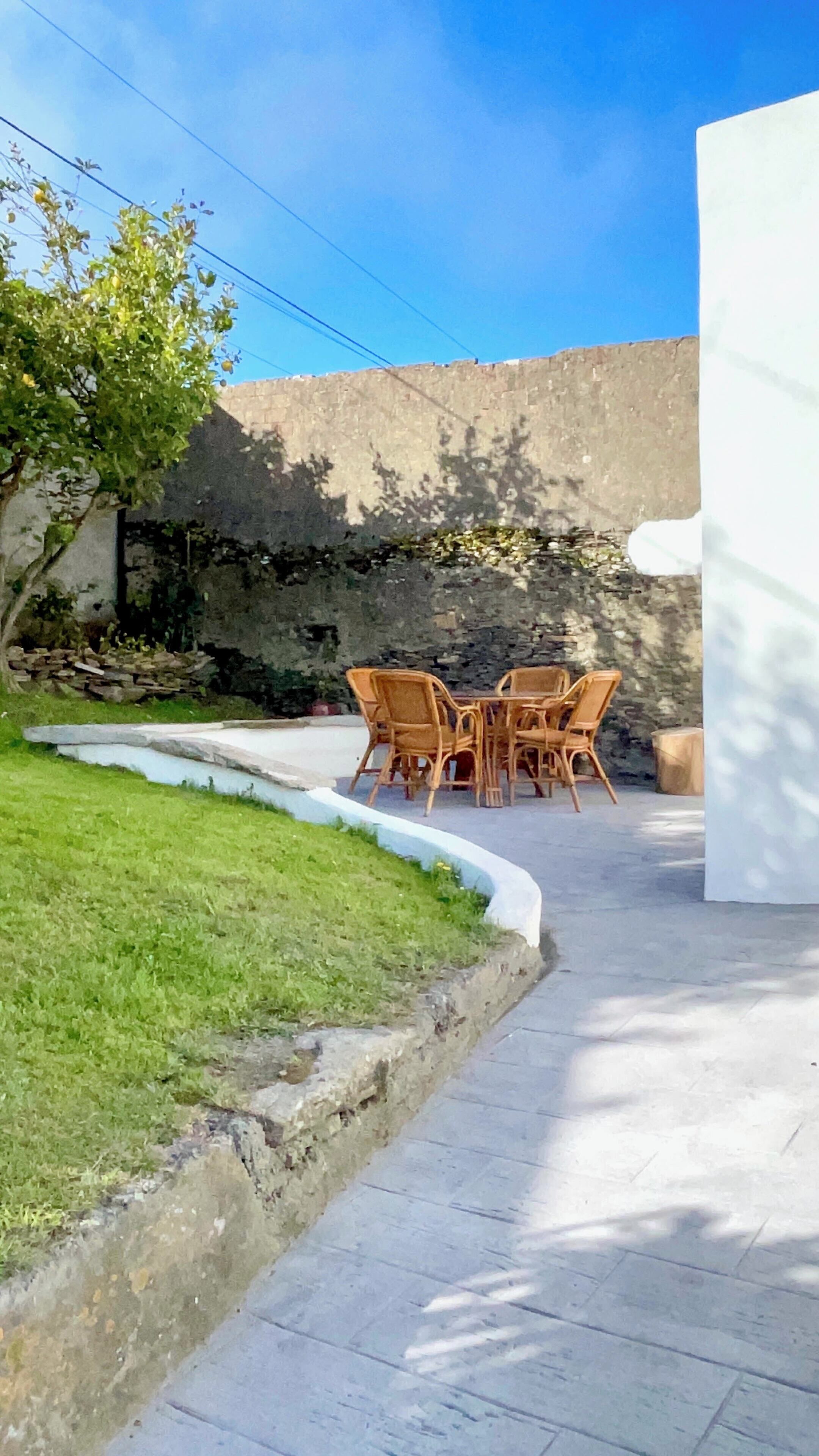 Un espace extérieur aménagé avec un mur en pierre, une pelouse et une table entourée de chaises.